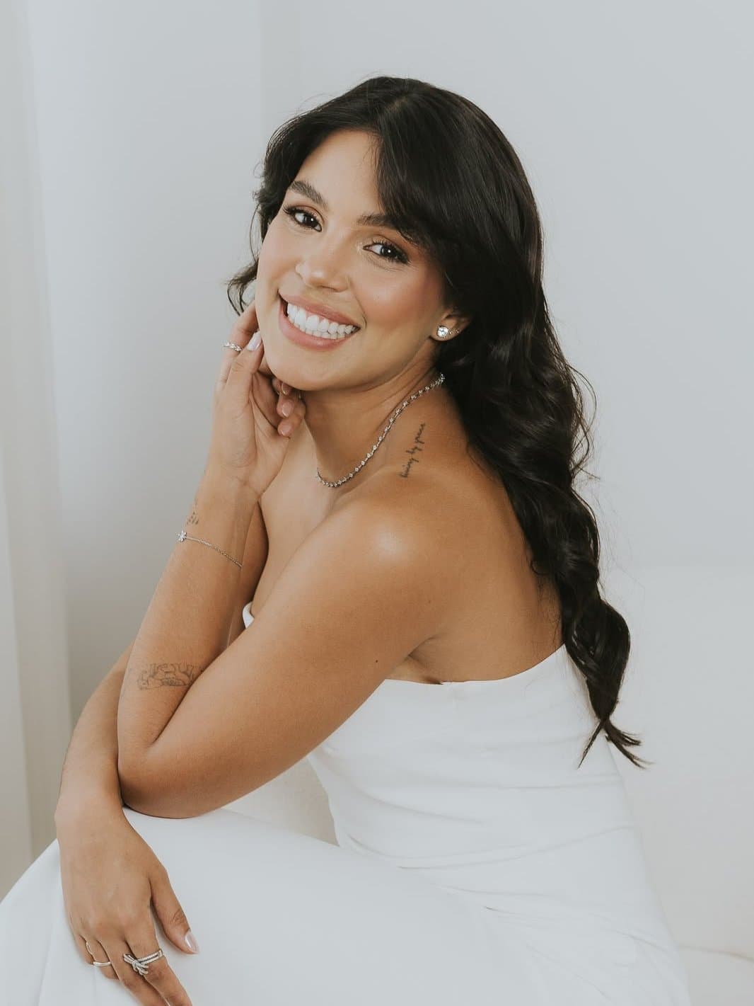 Retrato de Júlia Caixeta sonriendo, sentada, con vestido blanco