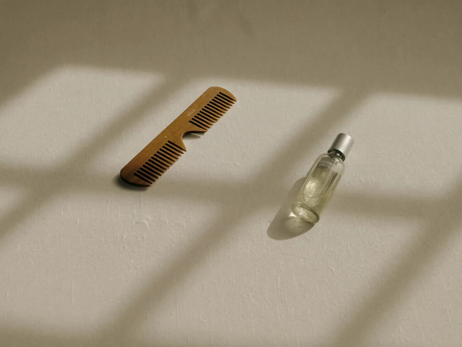 Peine de madera y un pequeño frasco de vidrio sin etiqueta sobre lino crudo, con la sombra de una ventana