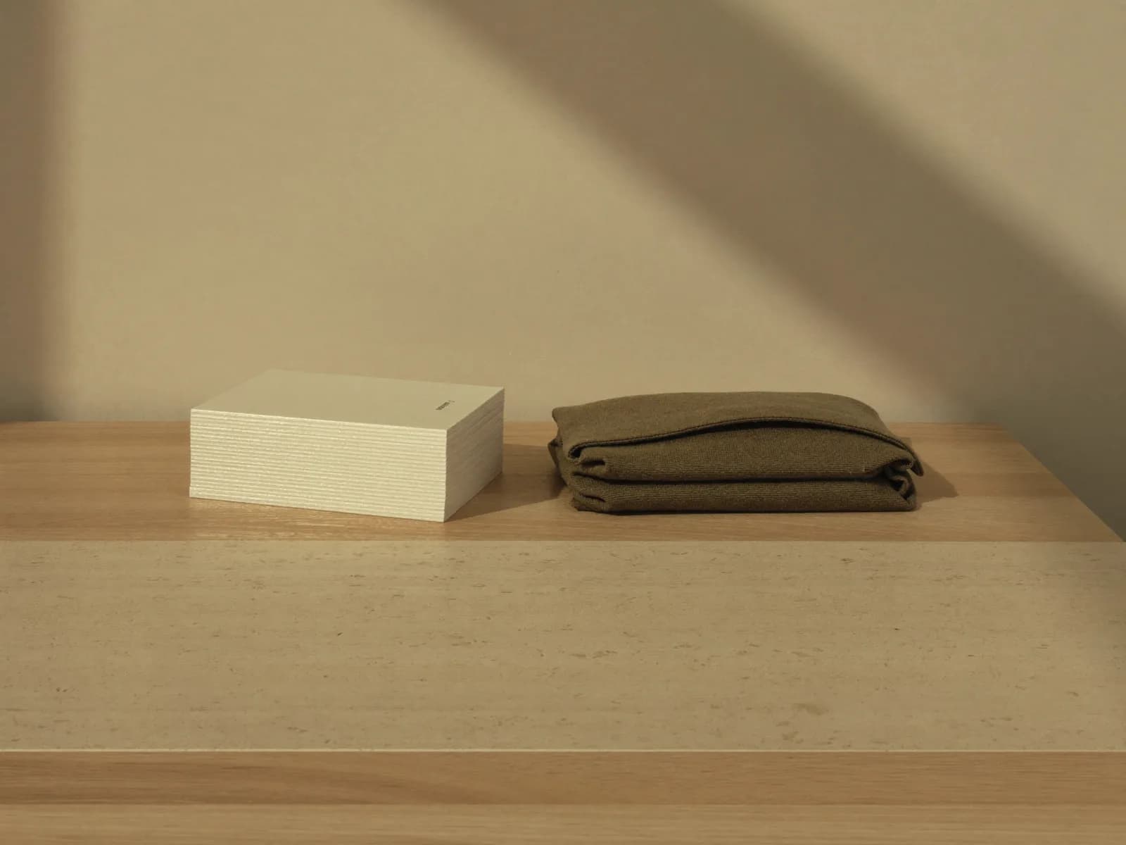 Pilha de cartões em branco ao lado de um pano dobrado sobre uma mesa de madeira clara, com a sombra de uma janela na parede