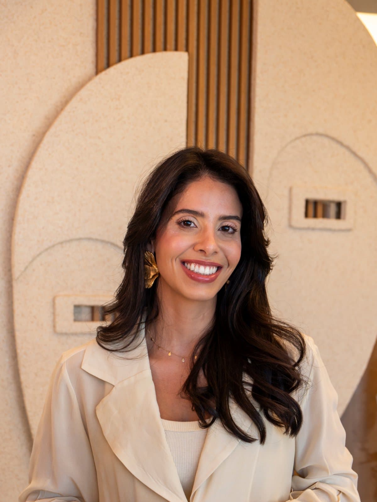 Dra. Mariana Barbosa sorrindo na recepção da Arco Clinic, diante do painel de madeira e pedra