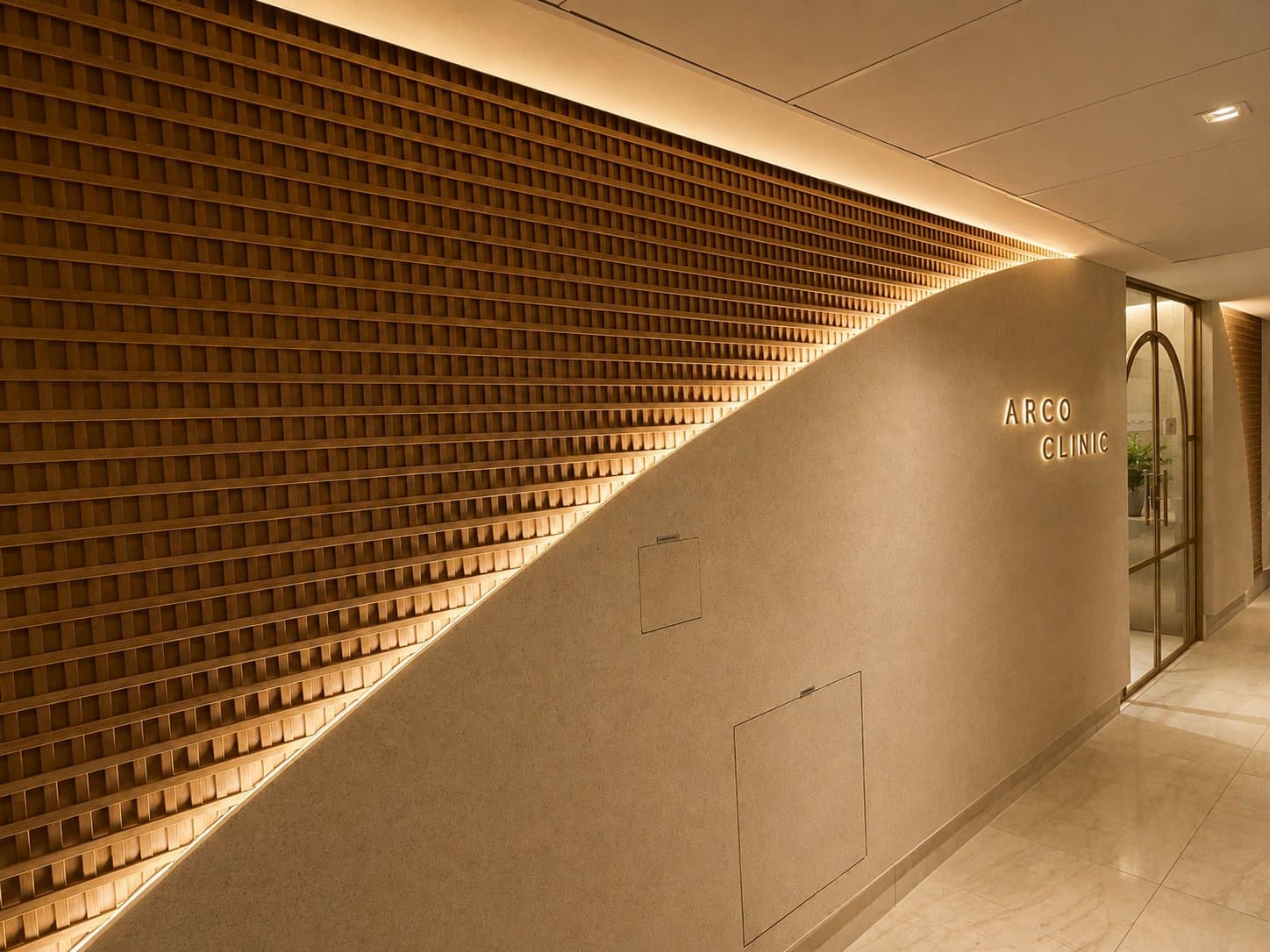 Parede curva de muxarabi da recepção, com o letreiro Arco Clinic iluminado