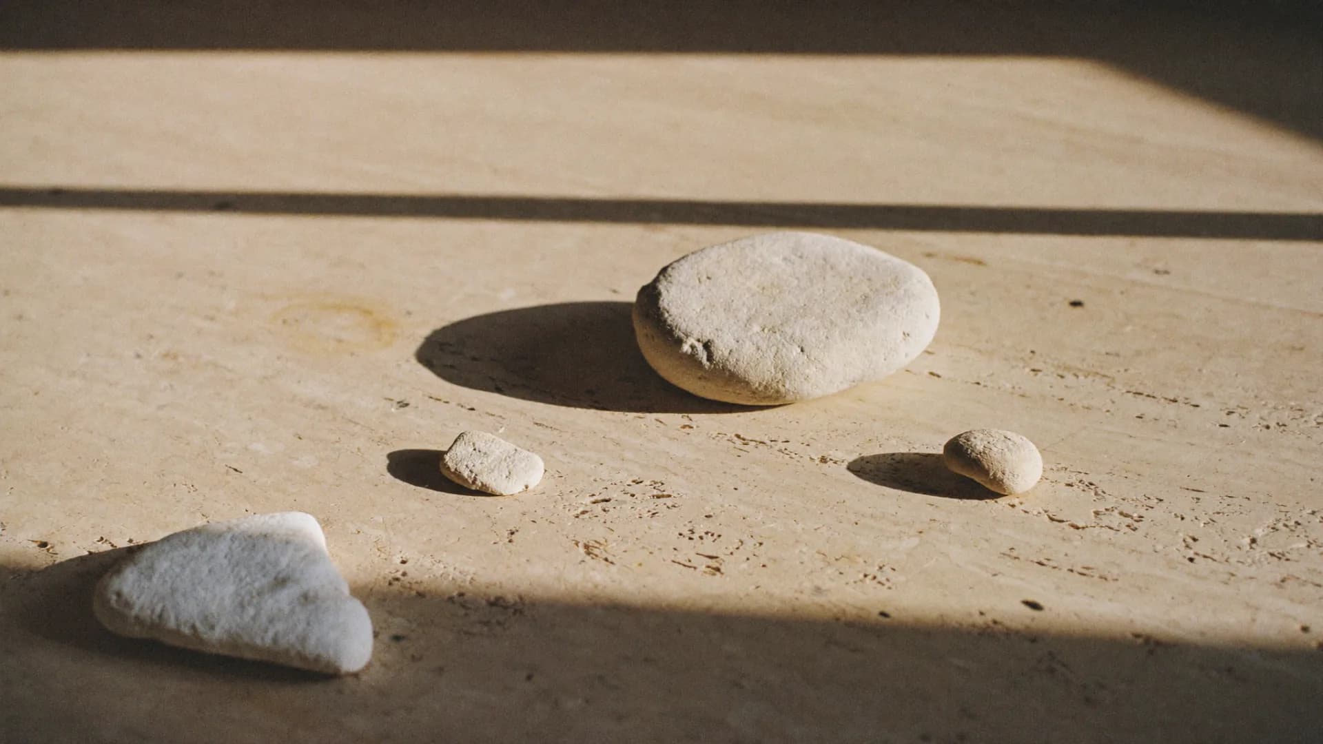 Tres piedras lisas de tamaño decreciente sobre una mesada de travertino, con luz cálida de ventana