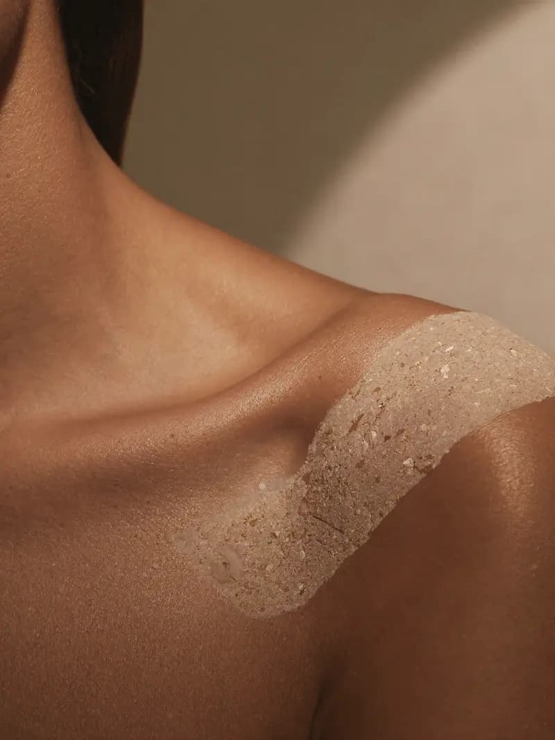 Detalle de hombro con textura mineral exfoliante sobre la piel, en luz cálida